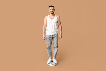 Fototapeta na wymiar Handsome sporty young man with scales on brown background. Weight loss concept