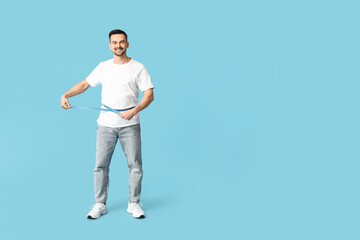 Fototapeta na wymiar Handsome sporty happy man measuring his waist on blue background. Weight loss concept