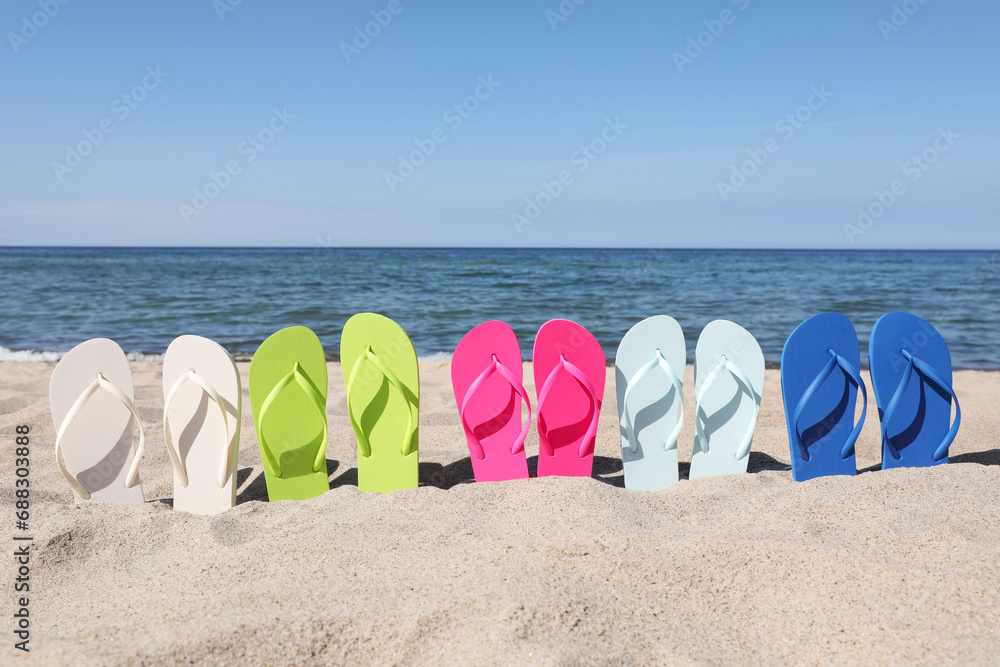 Poster Many stylish colorful flip flops on beach sand