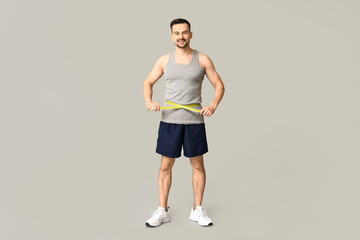 Fototapeta na wymiar Handsome sporty young man measuring his waist on grey background. Weight loss concept