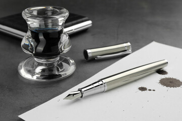 Stylish fountain pen, paper with blots of ink and inkwell on grey textured table