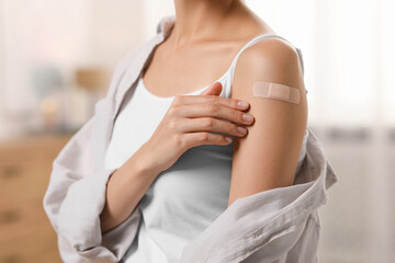 Woman with sticking plaster on arm after vaccination at home, closeup