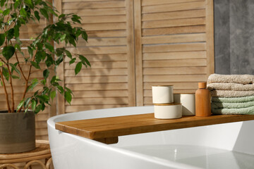 Wooden tray with spa products and towels on bath tub in bathroom. Space for text