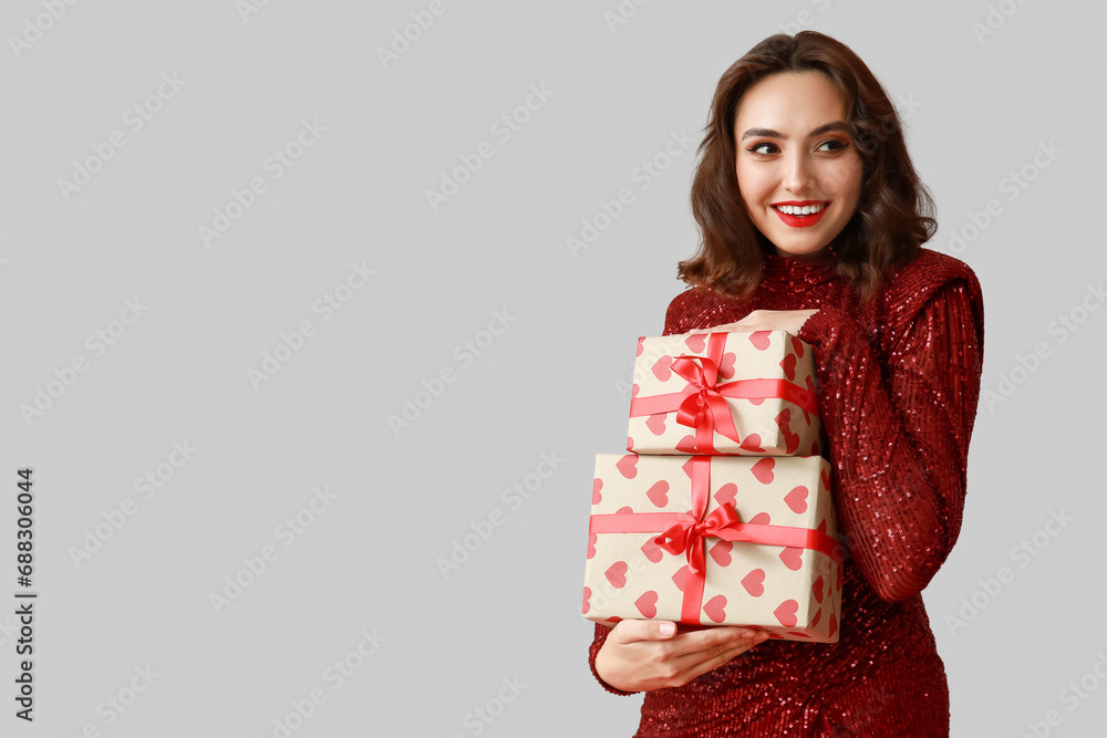 Sticker Beautiful young woman with gift boxes on grey background