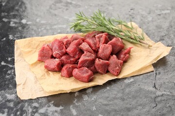 Pieces of raw beef meat and rosemary on grey textured table