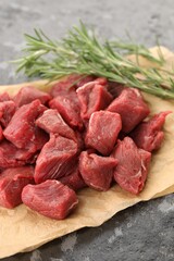 Pieces of raw beef meat and rosemary on grey textured table, closeup