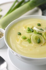 Bowl of tasty cream soup with leek on white table, closeup