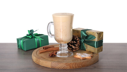 Delicious eggnog in glass, spices and gift boxes on wooden table against white background