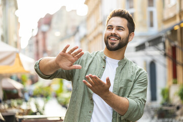 Cheerful rich bearded young man showing wasting throwing money around hand gesture, more tips earnings, big profit, win lottery, share, celebrate outdoors. Caucasian guy standing in urban city street - obrazy, fototapety, plakaty