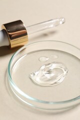 Pipette and petri dish with sample of cosmetic serum on beige background, closeup