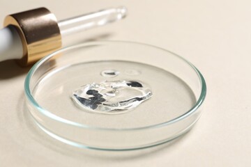 Pipette and petri dish with sample of cosmetic serum on beige background, closeup