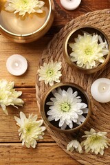 Fototapeta na wymiar Tibetan singing bowls, beautiful chrysanthemum flowers and burning candles on wooden table, flat lay