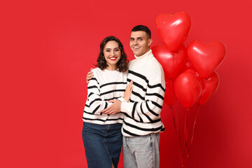 Loving young couple with heart-shaped balloons on red background. Celebration of Saint Valentine's Day
