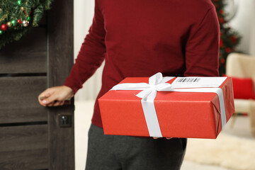 Young man in Santa hat with Christmas gift box received by mail indoors, closeup