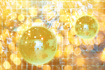 Shiny disco balls against foil party curtain under golden lights, bokeh effect