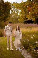 Fototapeta premium Young Cute Female Hugs Boyfriend. In Autumn Outdoor. Lovers Walking in Park. Attractive Funny Couple. Lovestory in Forest. Man and Woman. Cute Lovers in the Park. Family Concept. Happy Couple.
