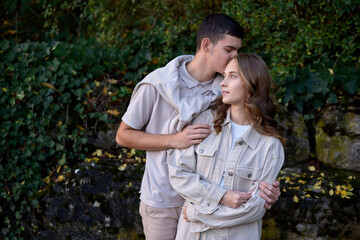 Fototapeta premium Young Cute Female Hugs Boyfriend. In Autumn Outdoor. Lovers Walking in Park. Attractive Funny Couple. Lovestory in Forest. Man and Woman. Cute Lovers in the Park. Family Concept. Happy Couple.
