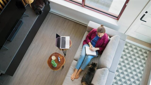 Overhead view of woman writing notes, lying on couch at home
