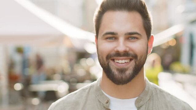 Portrait of happy bearded adult man smiling friendly, glad expression looking at camera dreaming, resting, relaxation feel satisfied good news outdoors. Guy in urban city sunny street background