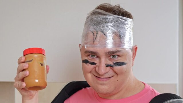 Portrait of man with war paint, ridiculous look, holding jar of peanut butter in his hands, decisively attacking Father playfully trying to feed children, family entertainment, fun games childishness