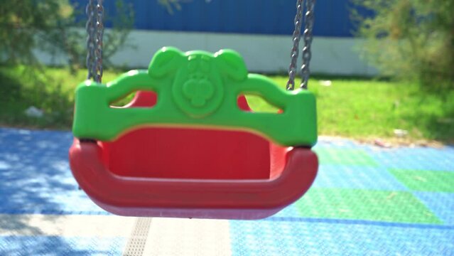 Empty bright plastic swings on playground in public city park on sunny day Attraction, entertainment for game, place for walks in kindergarten Protection, childhood safety, missing children kidnapping