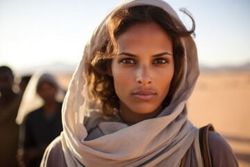 Serious young muslim middle eastern woman wearing a religious headscarf walking in the desert looking at the camera - obrazy, fototapety, plakaty