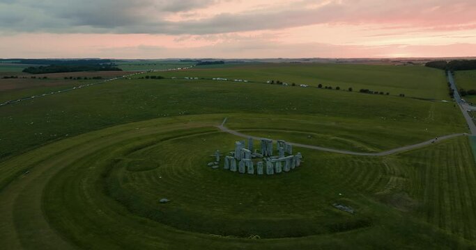 Cinematic shot of the famous Stonehenge and surrounding green meadows in in the sunset glow