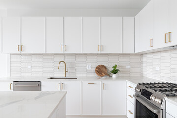 A beautiful kitchen detail with white cabinets, a gold faucet, white marble countertops, and a...