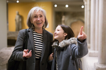 Friendly elderly female tutor showing interested tween girl exposition of artworks in museum of archeology and ancient sculptures - obrazy, fototapety, plakaty