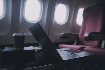 Attractive asian female passenger of airplane sitting in comfortable seat listening music in earphones while working at modern laptop computer with mock up area using wireless connection on board.