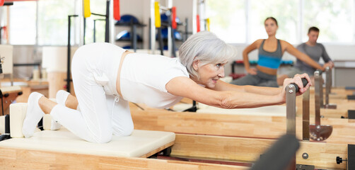 Senior woman works out in gym on Pilates simulator. Sports club client performs exercise on...