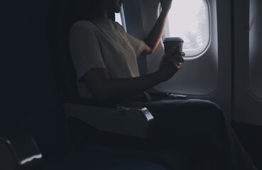 Asian woman enjoying enjoys a coffee comfortable flight while sitting in the airplane cabin, Passengers near the window.