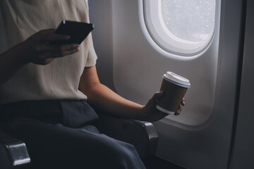 Asian woman enjoying enjoys a coffee comfortable flight while sitting in the airplane cabin, Passengers near the window.