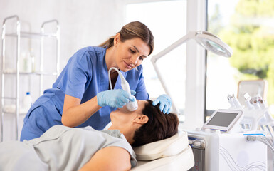 Female cosmetologist performing female face skin massage procedure in cosmetology clinic