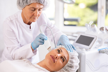 Young woman undergoing hardware cosmetic treatment for facial care in aesthetic medicine clinic, using ultrasonic shovel to cleanse skin, soften and remove excess keratin, boost collagen production