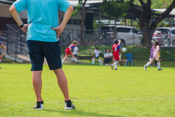 Dad standing and watching his son playing football in a school tournament on a sideline with a sunny day. Sport, outdoor active, lifestyle, happy family and soccer mom and soccer dad concept.