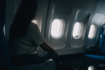 Silhouette of woman looks out the window of an flying airplane. Passenger on the plane resting...