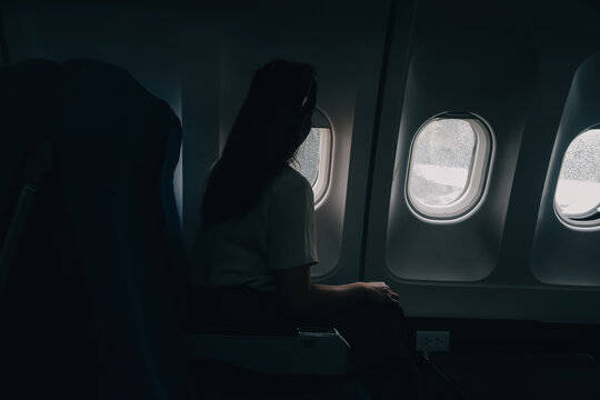Silhouette of woman looks out the window of an flying airplane. Passenger on the plane resting beside the window.