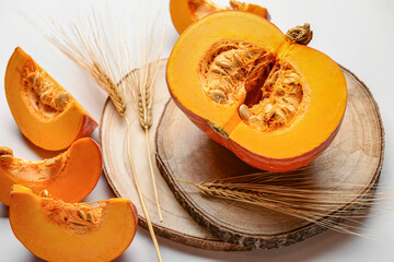 Wooden board with cut fresh pumpkin and wheat spikelets on beige background