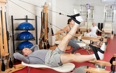 Adult man in sportswear training her legs with straps in pilates studio..