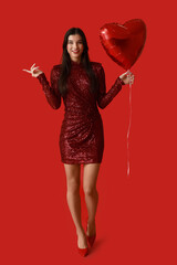 Beautiful young woman with kiss marks on her face and heart shaped air balloon pointing at something on red background