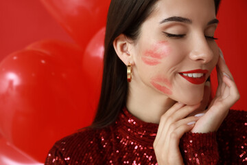 Beautiful young woman with kiss marks on her face and air balloons on red background