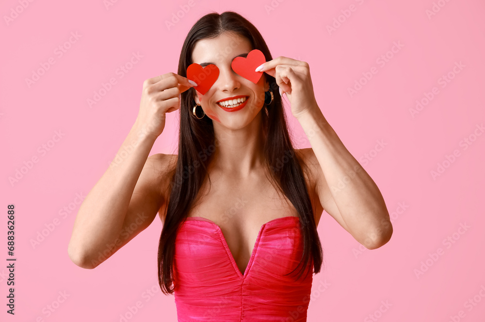 Poster Beautiful young woman with kiss marks on her face and red paper hearts on pink background