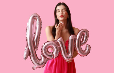 Beautiful young woman with kiss marks on her face and air balloons in shape of word LOVE on pink background