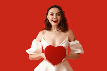Beautiful young woman with heart shaped gift box on red background