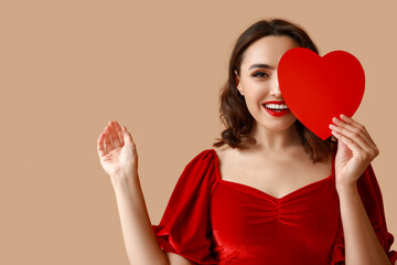 Beautiful young woman with red paper heart on brown background