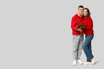 Loving young couple with bouquet of beautiful roses on grey background. Celebration of Saint...