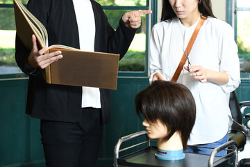 ヘアマネキンでヘアカット練習中に怒られる女性美容師と怒る男性美容師