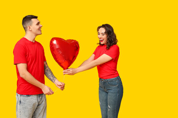 Loving young couple with heart-shaped balloon on yellow background. Celebration of Saint...