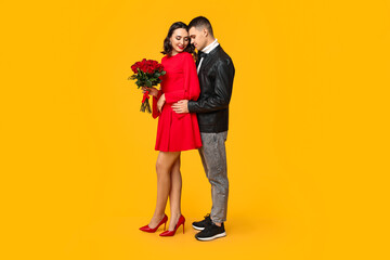 Loving young couple with bouquet of beautiful roses on yellow background. Celebration of Saint Valentine's Day